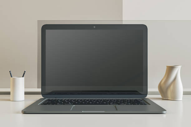 istock Front view on blank dark modern laptop monitor screen with place for web design or web page on white surface table among stand for pens and vase on light wall background. 3D rendering, mockup 1472292398