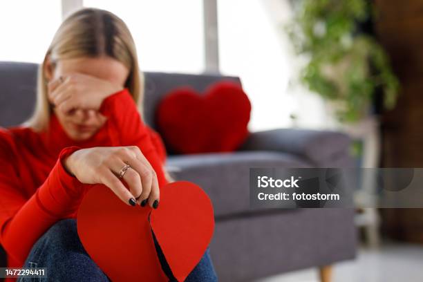 Sad Young Woman Holding A Broken Heart Made Out Of Paper And Crying Stock Photo - Download Image Now
