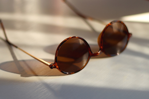 Round brown sunglasses on the table, illuminated by sunlight. Selective focus.