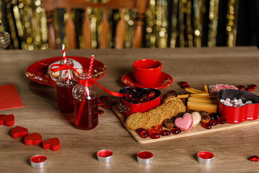 Close up shot of a delicious sweet charcuterie board and red colored drinks served on a table for a Valentine's day celebration.