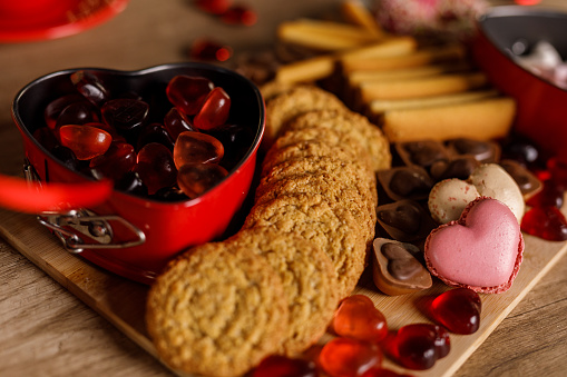 Close up shot of a delicious sweet charcuterie board filled with cookies, heart shaped candy and macaroons, set up on the table for a Valentine's day celebration.