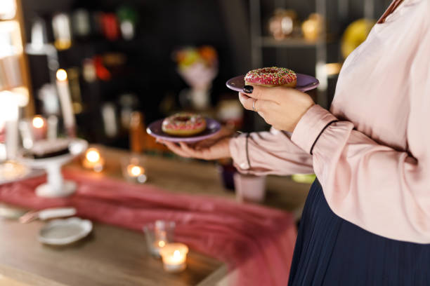 istock Young woman serving plates with pink colored doughnuts on the table 1472297698