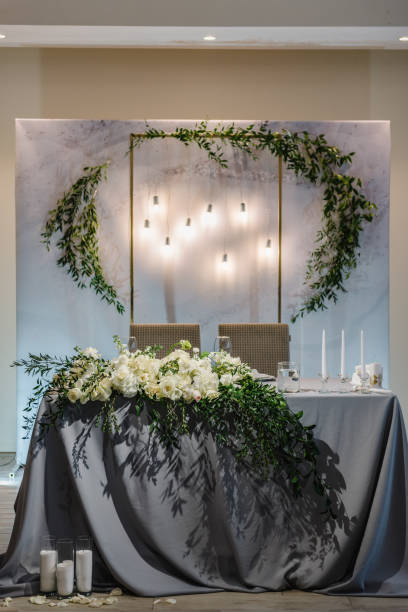 istock Festive table with arch decorated composition flowers and greenery, candles in hall restaurant. Table newlyweds covered with a tablecloth in banquet area on wedding party. Table setting, reception. 1472299096