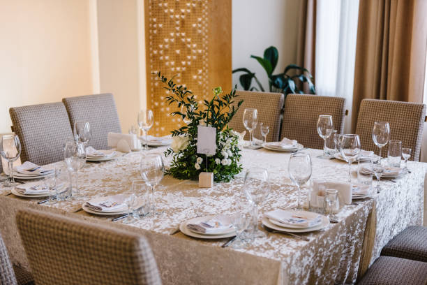 istock Wedding set up, dinner table reception. A plate with a napkin, knives and forks next to the plate. Flower composition with greenery leaves in center of table. Banquet decoration in hall restaurant. 1472299157