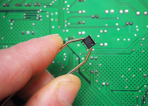 Hand holding a micro chip on electronic circuit board background. Semiconductor technology concept.