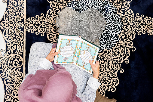 woman sitting in the mosque and reading muslim book with arabic calligraphy Quran translation :  holy book and verses text on a wooden stand