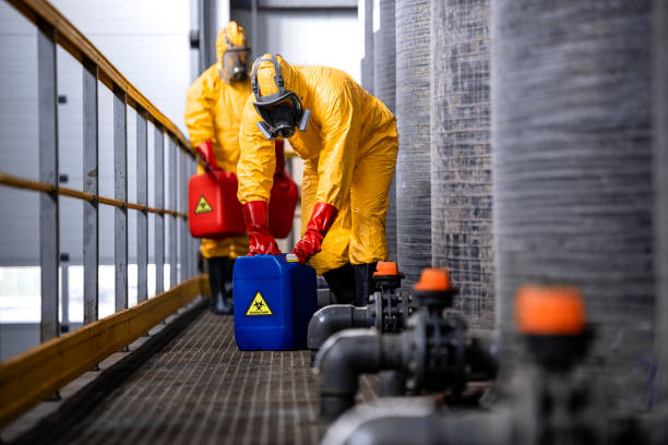 istock Experienced and trained workers with gas masks handling hazardous material inside chemicals factory. 1472300752