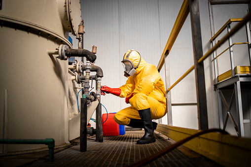 Factory worker filling canister with acid inside chemicals production plant.