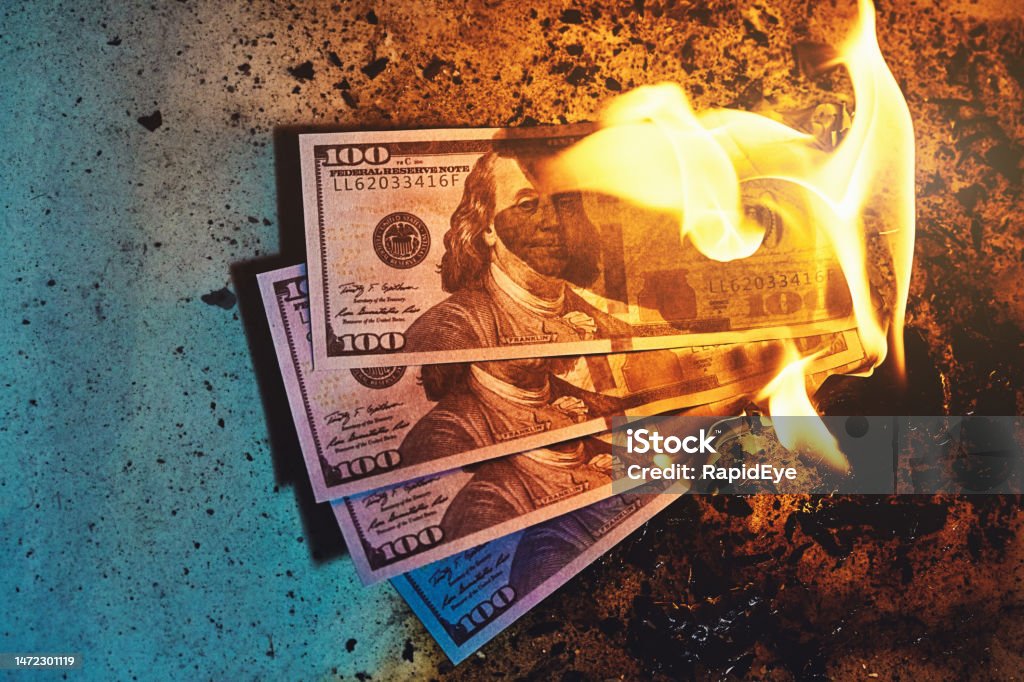 Three $100 banknotes burning, amid fire, flames and ash Money to burn: Three large-denomination US dollar banknotes going up in flames. Currency Stock Photo