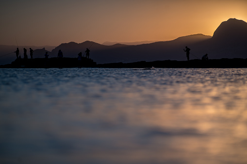 Fishermen fish in the sea during sunset against the backdrop of beautiful mountains and the setting sun