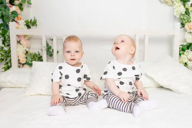 two baby twins 8 months old sitting on the bed in the same clothes, brother-sister relationship, fashionable clothes for children of twins