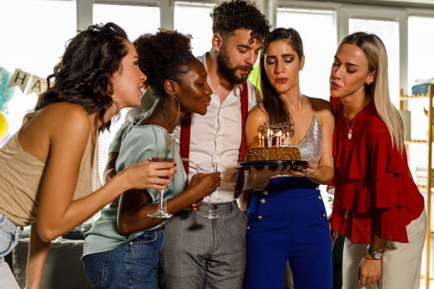 istock Young man surrounded with girlfriends blowing out candles on his birthday cake 1472302885