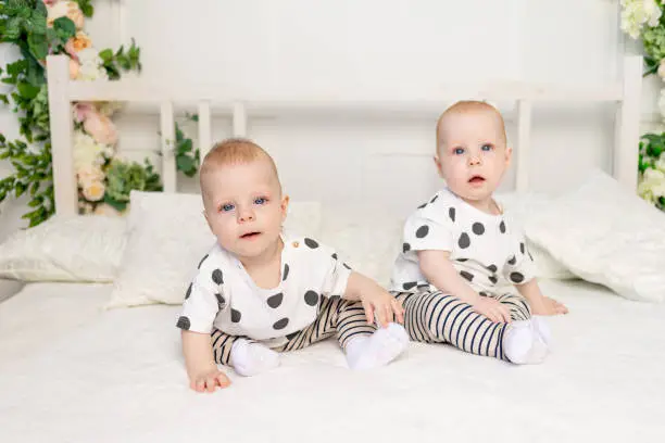 two baby twins 8 months old sitting on the bed in the same clothes, brother-sister relationship, fashionable clothes for children of twins, concept of marriage and friendship