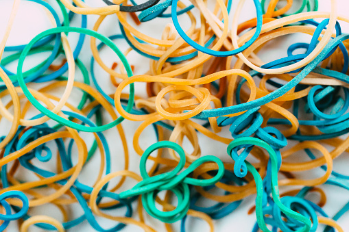Macro close up color image depicting a collection of colored rubber bands on a white background.