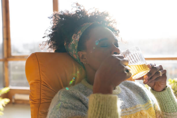 Enjoying a Cup of Tea Woman relaxing laying in a chair drinking a cup of tea at her home in the North East of England. She has her eyes closed and the sun is shining through the windows behind her. older woman eyes closed stock pictures, royalty-free photos & images