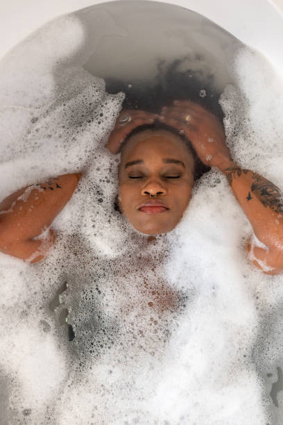 Washing her Hair in the bath Direct above shot of a woman in a bubble bath relaxing with her eyes closed at her home in the North East of England. black woman washing hair stock pictures, royalty-free photos & images