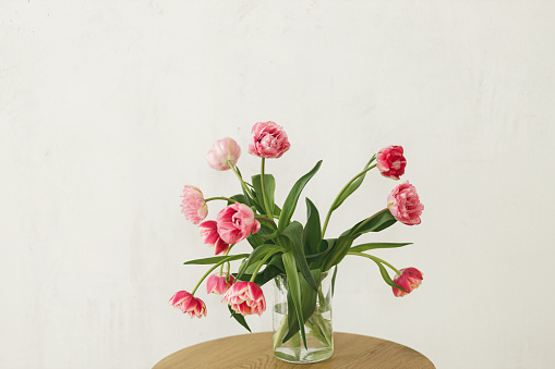 Stylish beautiful pink tulips bouquet in vase on wooden table in rustic room. Floral arrangement in farmhouse. Spring flowers composition, copy space. Happy mothers day and womens