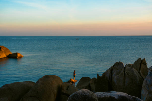 Young man fishing while standing on rocks on Koh Samui Island