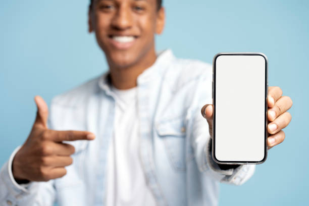 istock Smiling young guy points index finger at empty smartphone screen isolated on blue background 1472317752