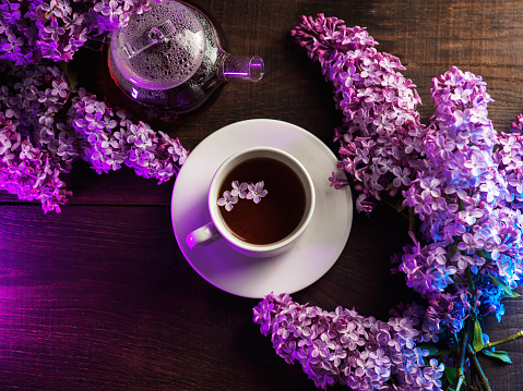 Top view of a cup of tea on a wooden table. Flowering bouquet of lilacs, teapot with lilac flowers. healthy tea