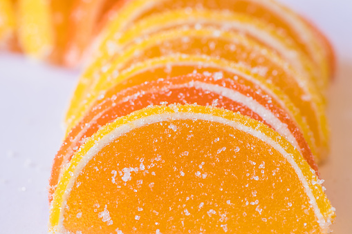 Decorative Background of yellow and orange marmalade candy in the shape of citrus fruits wedges. Jelly sweet candies. Food Texture. Beautiful marmalade lemon wedges white background.
