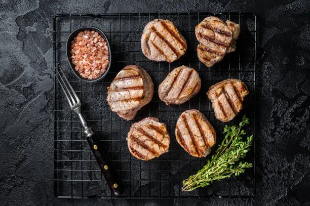 Grilled pork medallions steaks from tenderloin meat on a rack. Black background. Top view.