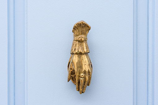 Paraty, Brazil. Antique gilded brass knocker in the shape of a hand on a lilac wooden door.