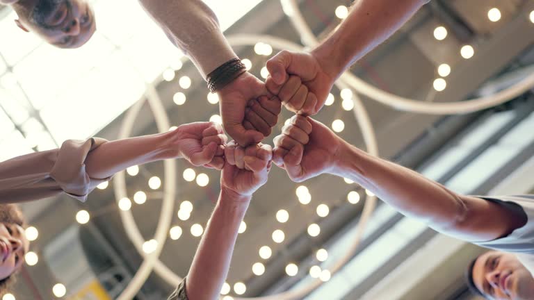 Fist bump, teamwork and business people doing team building, celebration or collaboration in workplace. Hands, bottom view and group of employees celebrating success, achievement or goal in office.