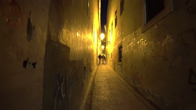 Tourist POV - narrow pathway between old buildings with old streetlamp that emit warm light at nighttime in Zagreb, Croatia