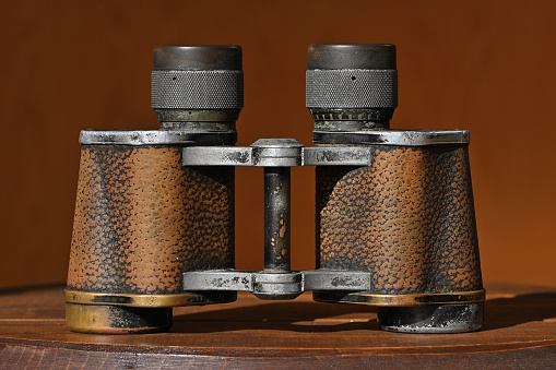 Vintage binoculars on wooden stool in sunlight. These are World War II-era 8x30 Zeiss binoculars made in Jena, Germany -- battered and with much of the black finish worn away.