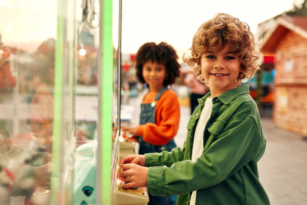 Children play in the arcade center of the machine to get the claws of soft toys for coins. An African-American girl and a cute curly Caucasian boy at amusement park.
