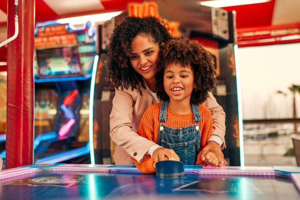 Kids having fun on a carnival Carousel A cute African-American child with afro curls with her mother playing air hockey at an amusement park and carousel on her day off in the evening. arcade stock pictures, royalty-free photos & images