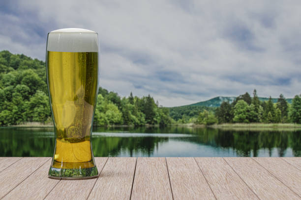 Glass of light beer on table with view of forest with lake stock photo