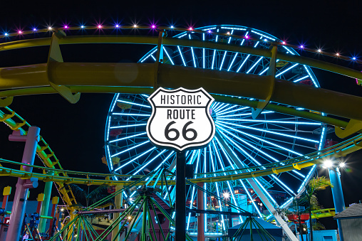 Los Angeles, United States - November 17, 2022: A picture of the Route 66 sign at night, with the Pacific Wheel in the back.