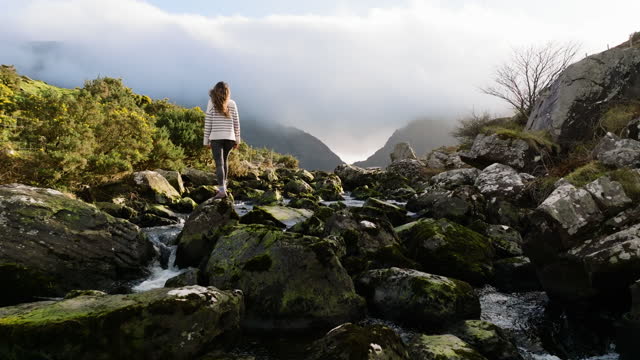 Aerial view of Gap of Dunloe, County Kerry in Ireland, woman watching nature under the old stone bridge, being free in nature, strong woman in nature, woman saluting nature, cinematic nature video, relaxation meditation nature