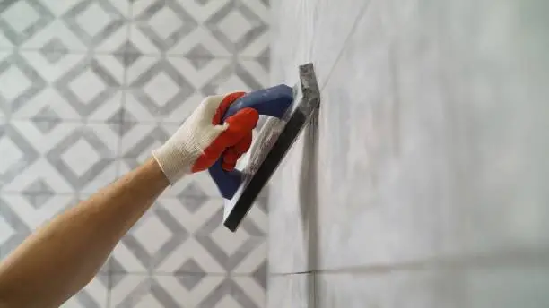 Photo of Black grout for tiles. laying ceramic tiles. Tilers fill the spaces between tiles with a rubber trowel. Grout in the bathroom.