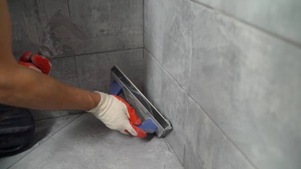 istock Grouting ceramic tiles. Tilers filling the space between tiles using a rubber trowel. Grouting ceramic tiles on the floor with a rubber trowel. Grouting tiles seams with a rubber trowel. 1472348862