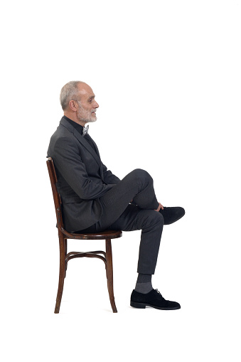 side view of a man sitting  on chair with suit and tie bow with cross legged on white background