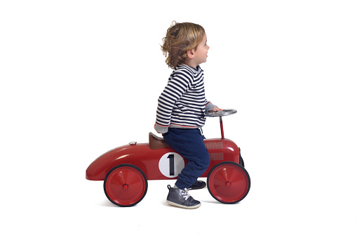 side view of a baby boy playing with car toy on white background