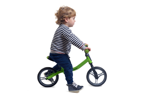 side view of a baby boy bicycling a bicycle on white background