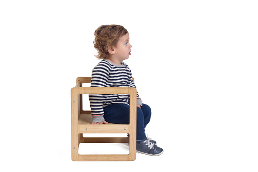 side view of a baby boy sitting on chair on white background