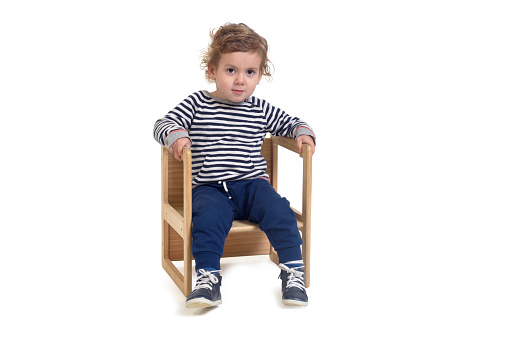 front view of a baby boy sitting on chair  and looking at camera on white background