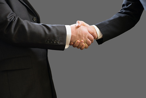 Business handshake of two businessmen in suits isolated on grey background.