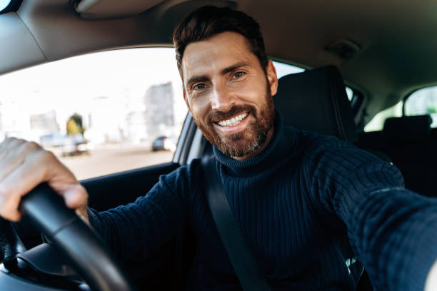Handsome bearded man holding camera and making selfie while sitting in the car stock photo