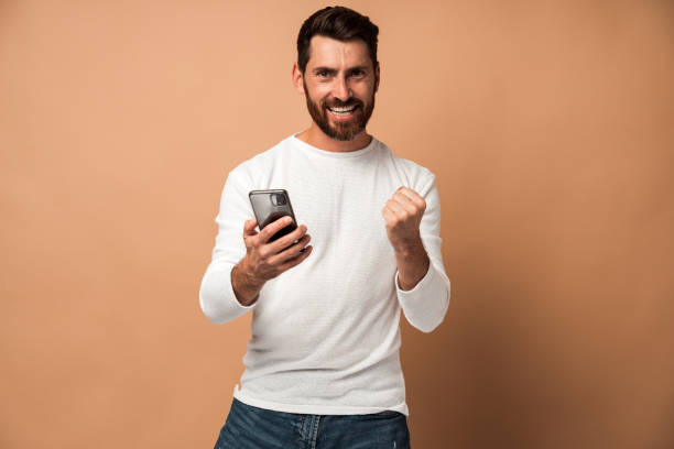 istock Attractive man with beard standing, holding phone and celebrate victory 1472353236