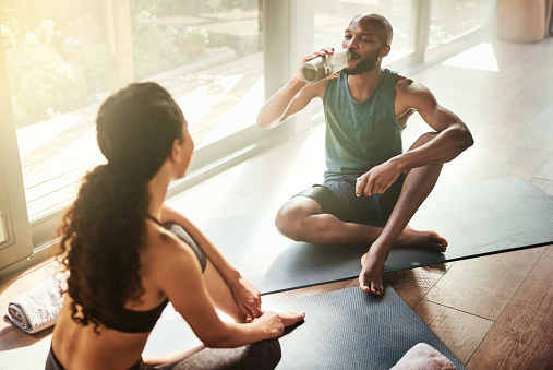Black man, yoga or friends drinking water to relax after exercise, group training or fitness workout together. Wellness, bonding or people talking, conversation or speaking in a discussion in studio