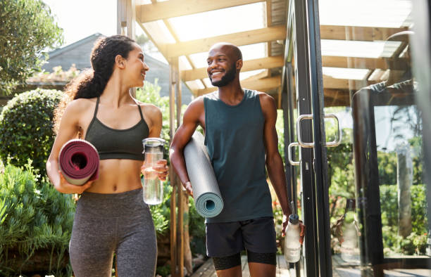 Interracial couple, outdoor and yoga exercise with smile for class, wellness and funny joke. Black man, woman and walk in garden, backyard or nature to studio for fitness, training and comic moment pareja interracial, ejercicio al aire libre y yoga con sonrisa para clase, bienestar y broma divertida. hombre negro, mujer y camina en el jardín, el patio trasero o la naturaleza al estudio para estar en forma, entrenar y momento cómico