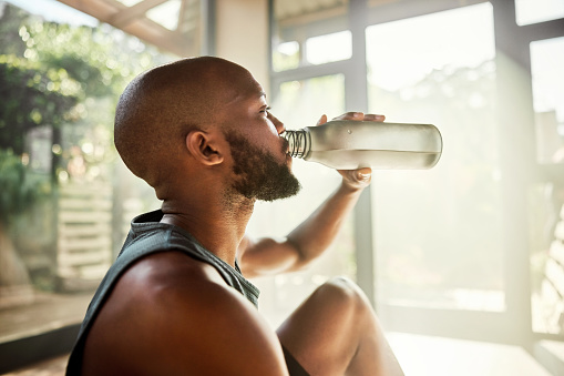 Drinking water, yoga and black man with a bottle after workout and wellness exercise. Relax, zen and drink for wellbeing in a home living room for meditation, pilates or zen practice at a house