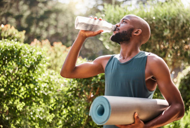 yoga mat, fitness and black man drinking water in nature for health and wellness outdoors. athlete, pilates and male yogi drink liquid for hydration after exercising, workout or training exercise. - water bottle water bottle drinking imagens e fotografias de stock