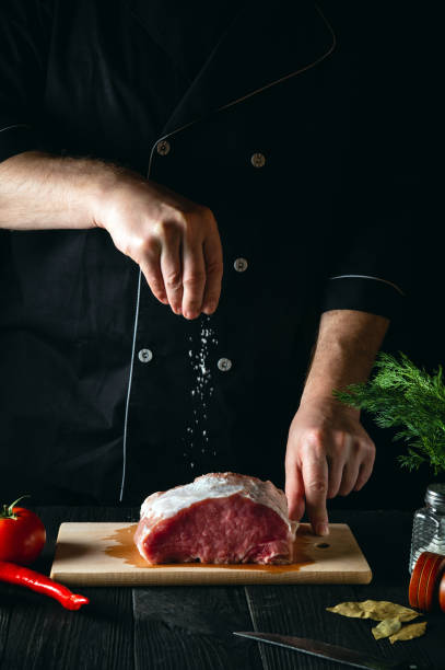 istock Chef sprinkles the meat with salt. Preparing meat before baking. Working environment in the kitchen of a restaurant or cafe 1472357123